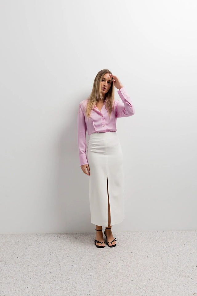 Femme stylée en chemise femme cintrée rose pastel et jupe midi fendue, posant élégamment dans un intérieur moderne.