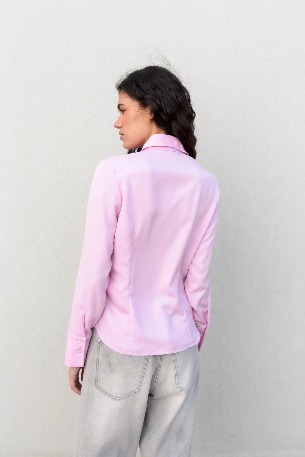 Détail de la chemise femme cintrée rose pastel sur une femme, montrant la coupe élégante et ajustée, vêtue d’un jean.