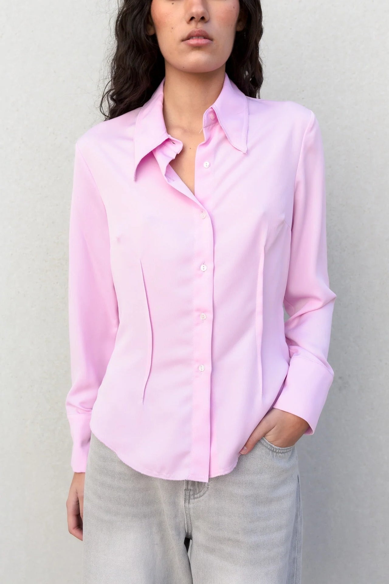Femme en chemise femme cintrée rose pastel, vêtue de pantalon blanc, marchant dans un décor urbain avec une allure chic.
