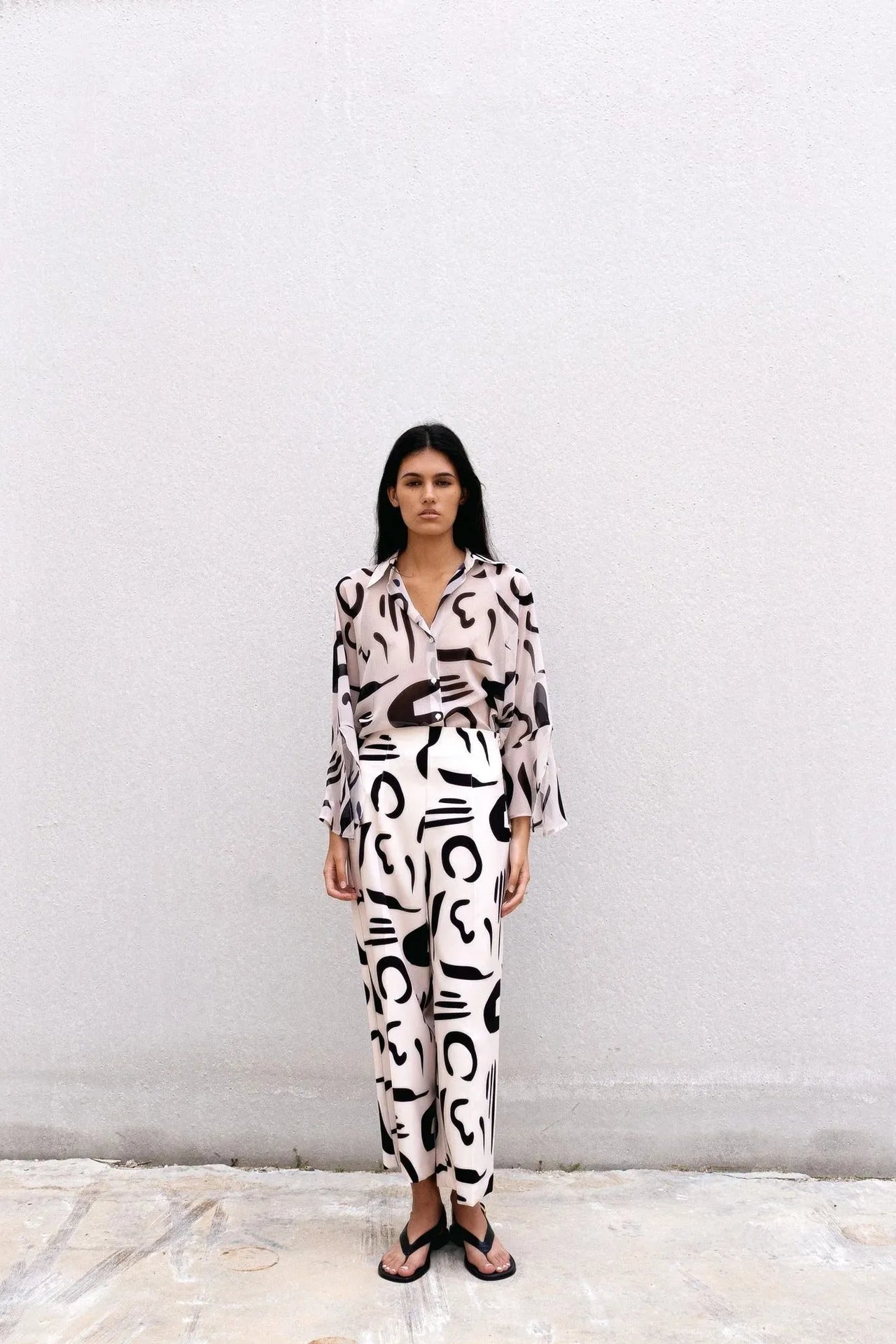 Femme portant un chemisier fluide imprimé noir et blanc, ensemble coordonné, sandales noires