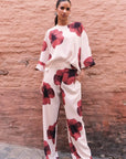 Chemisier Femme Chic Tendance Rouge Fleurie À Manches 3/4, modèle porté avec un pantalon assorti, affichant un imprimé floral vibrant sur fond clair.