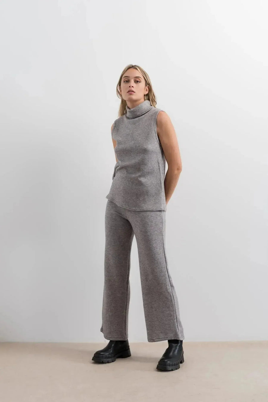 Femme montrant un gilet sans manche femme, habillée en ensemble col roulé et pantalon large gris pour un look moderne.