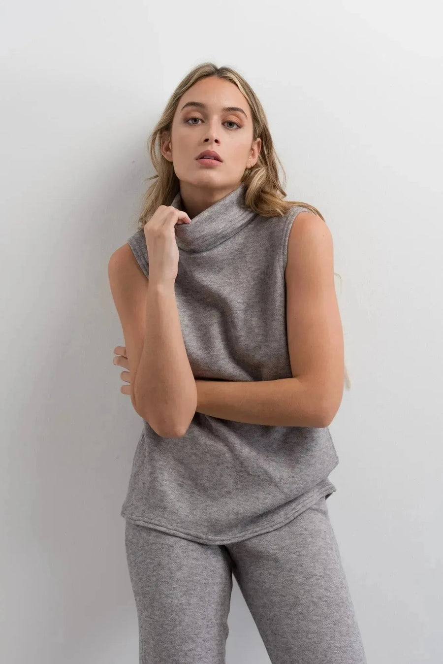 Femme posant avec un gilet sans manche femme sur un ensemble col roulé et pantalon large gris, montrant une allure chic.