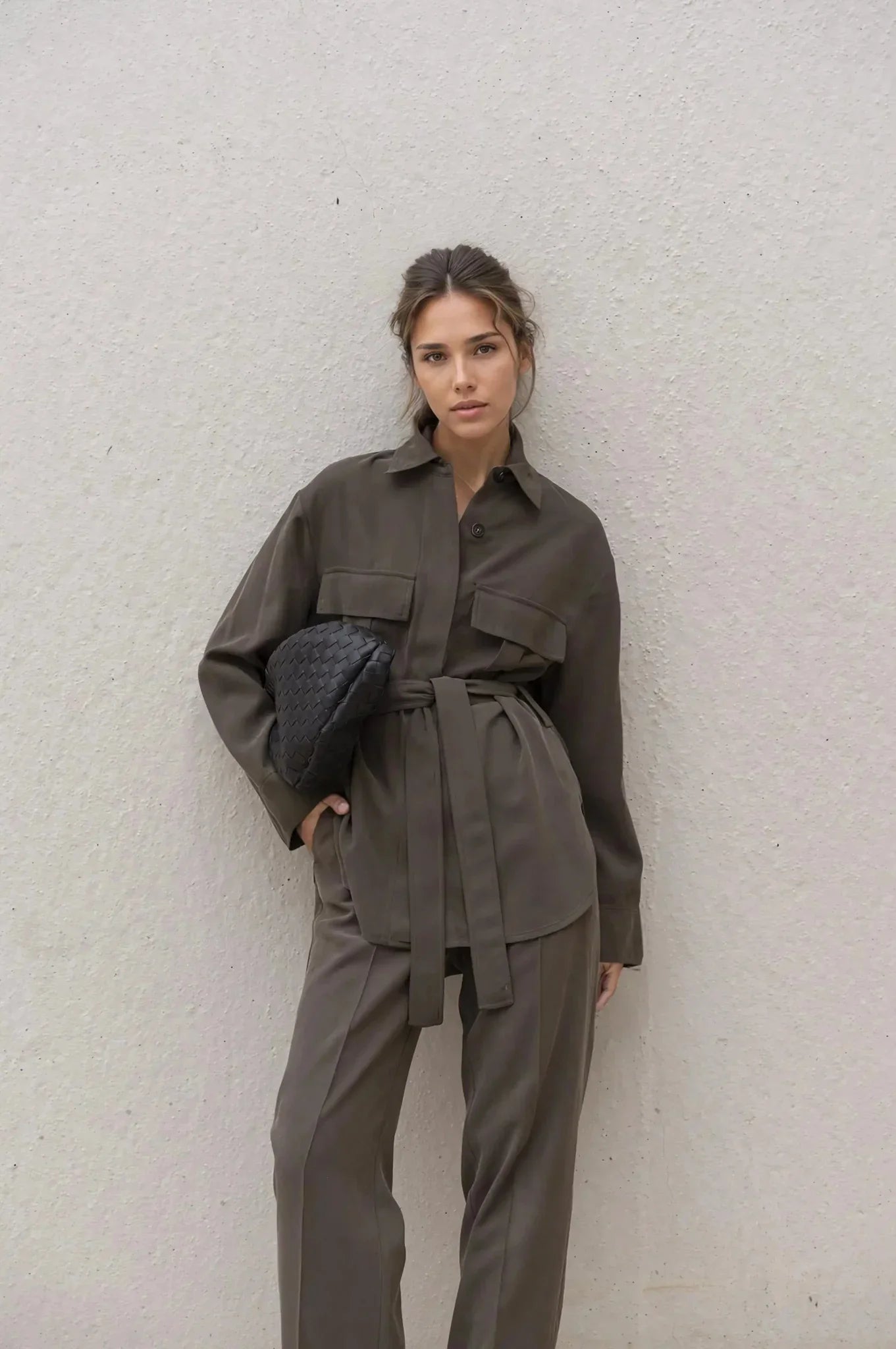 Femme portant un ensemble coordonné chemise et pantalon marron foncé avec sac clutch noir