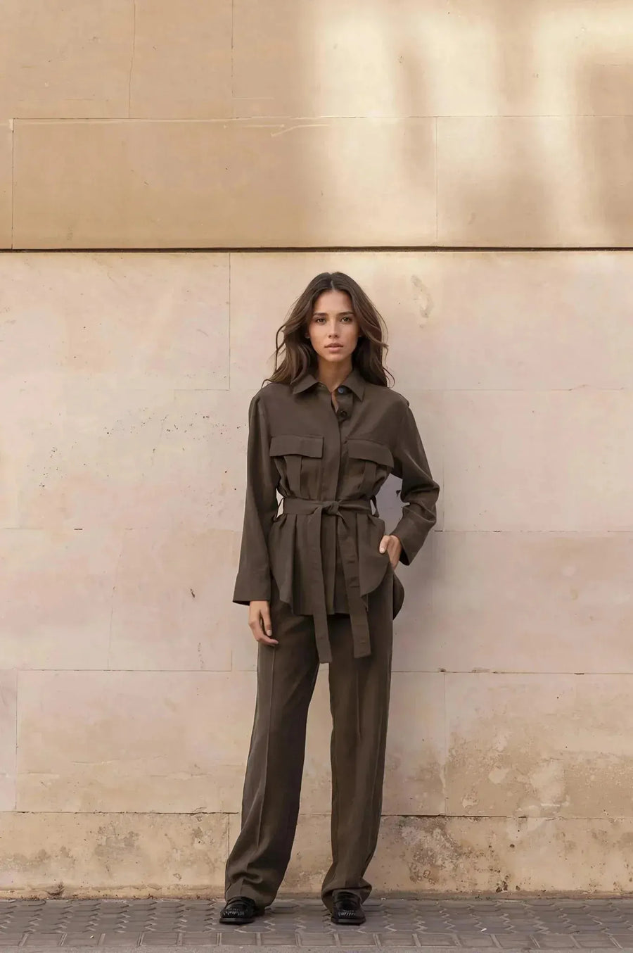 Ensemble coordonné chemise et pantalon kaki femme, pose élégante contre un mur en pierre.