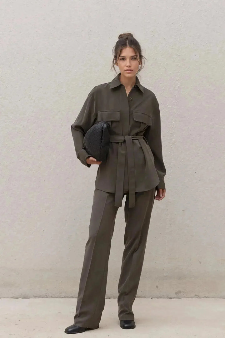 Ensemble coordonné chemise et pantalon kaki femme, modèle élégant avec ceinture, debout devant un mur neutre.