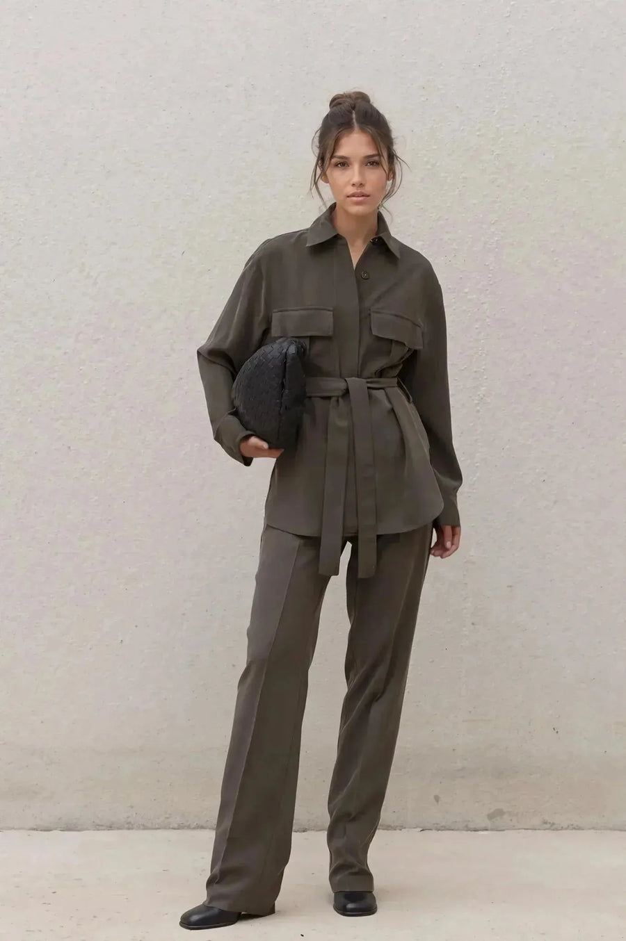 Ensemble coordonné chemise et pantalon kaki femme, modèle élégant avec ceinture, debout devant un mur neutre.