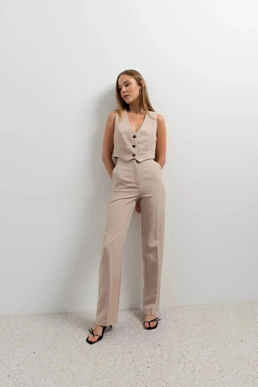 Femme en gilet de costume femme court beige élégant et confortable, se tenant contre un mur, illustrant un look tendance et sophistiqué. Idéal pour toute occasion.