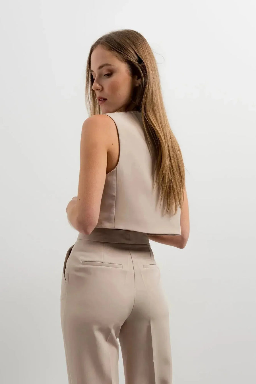Femme montrant le dos de son gilet de costume femme court beige élégant et confortable, mettant en valeur sa silhouette. Une pièce à porter en toute occasion.