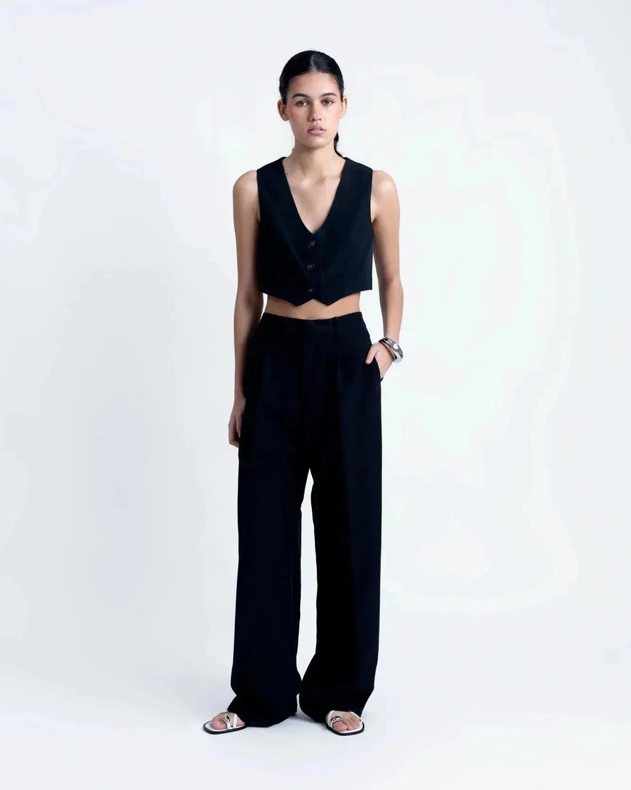 Modèle présentant un gilet costume femme court avec boutons, assorti à un pantalon noir pour un look chic.
