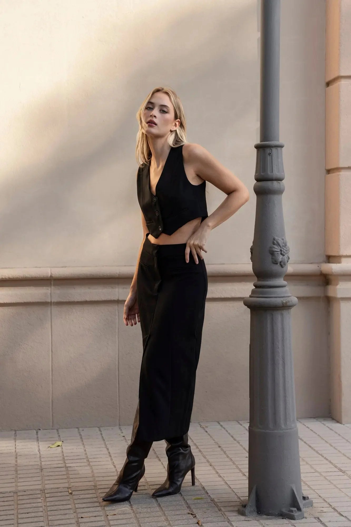Femme debout avec une jupe noire fendue et un top chic, affichant une allure élégante dans un cadre urbain.