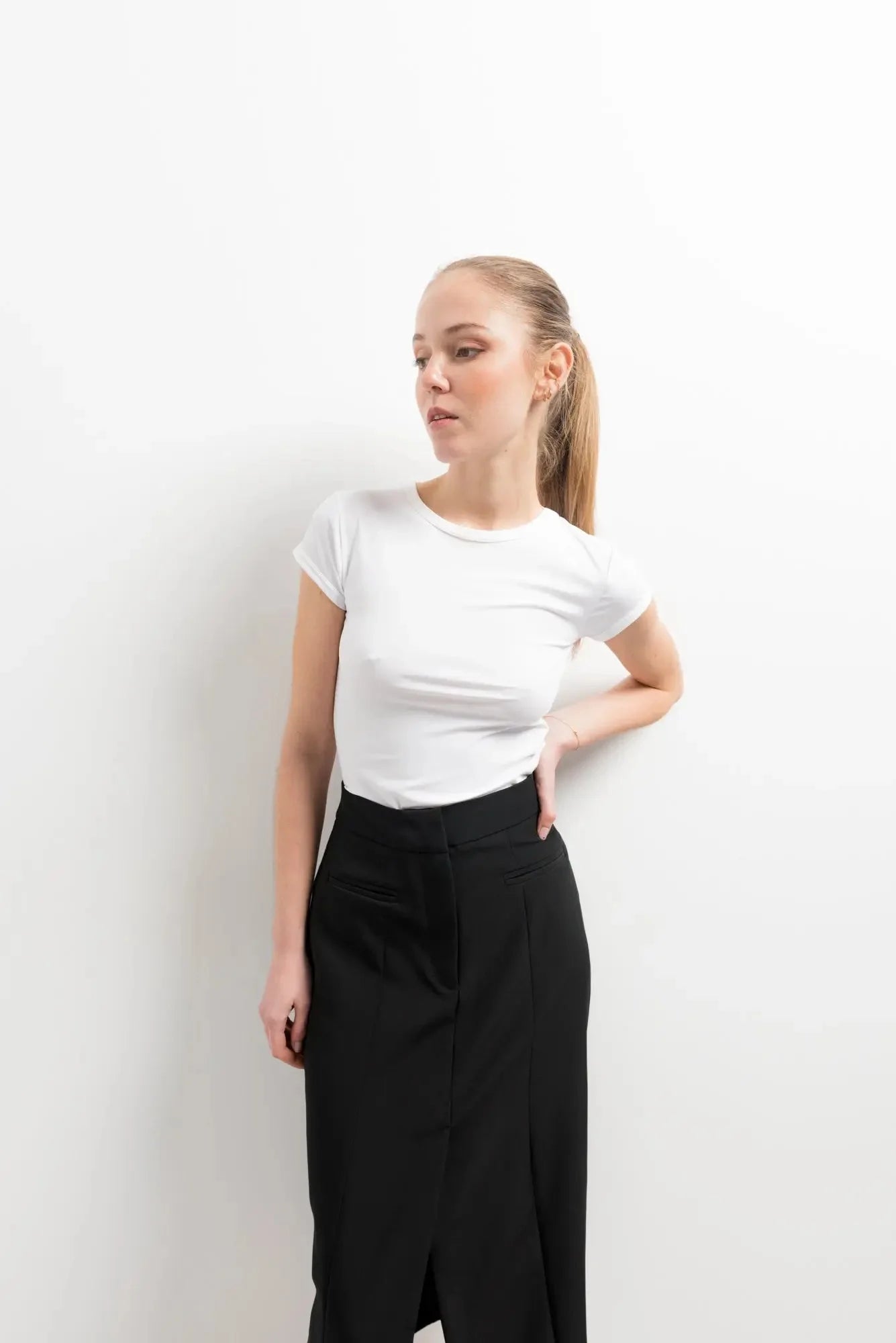 Close-up sur une femme en jupe noire fendue et t-shirt blanc, dégageant une élégance moderne.