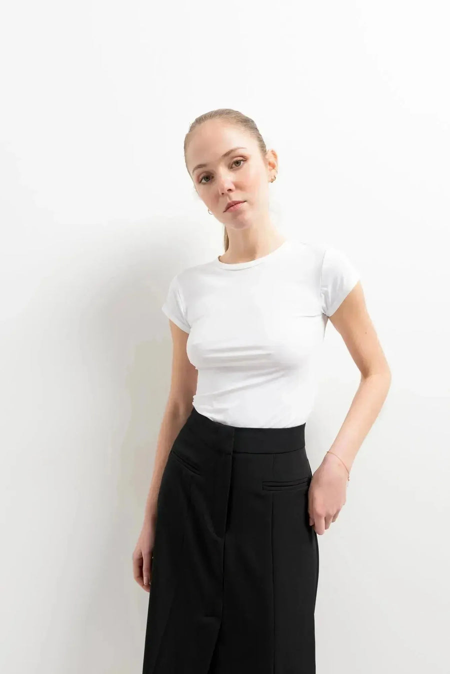 Femme présentant une jupe noire fendue avec un t-shirt blanc, capturant la tendance moderne avec simplicité.