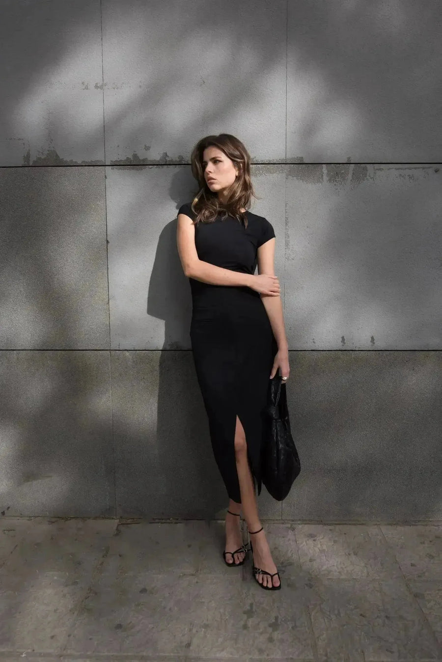 Femme posant avec une jupe noire fendue, exhalant un style chic et tendance dans un environnement contemporain.