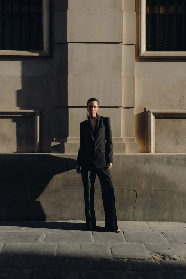 Image captivante d'un modèle dans le Pantalon Noir Fluide Femme Élégant à Pinces en Polyester Recyclé, baigné de lumière naturelle.