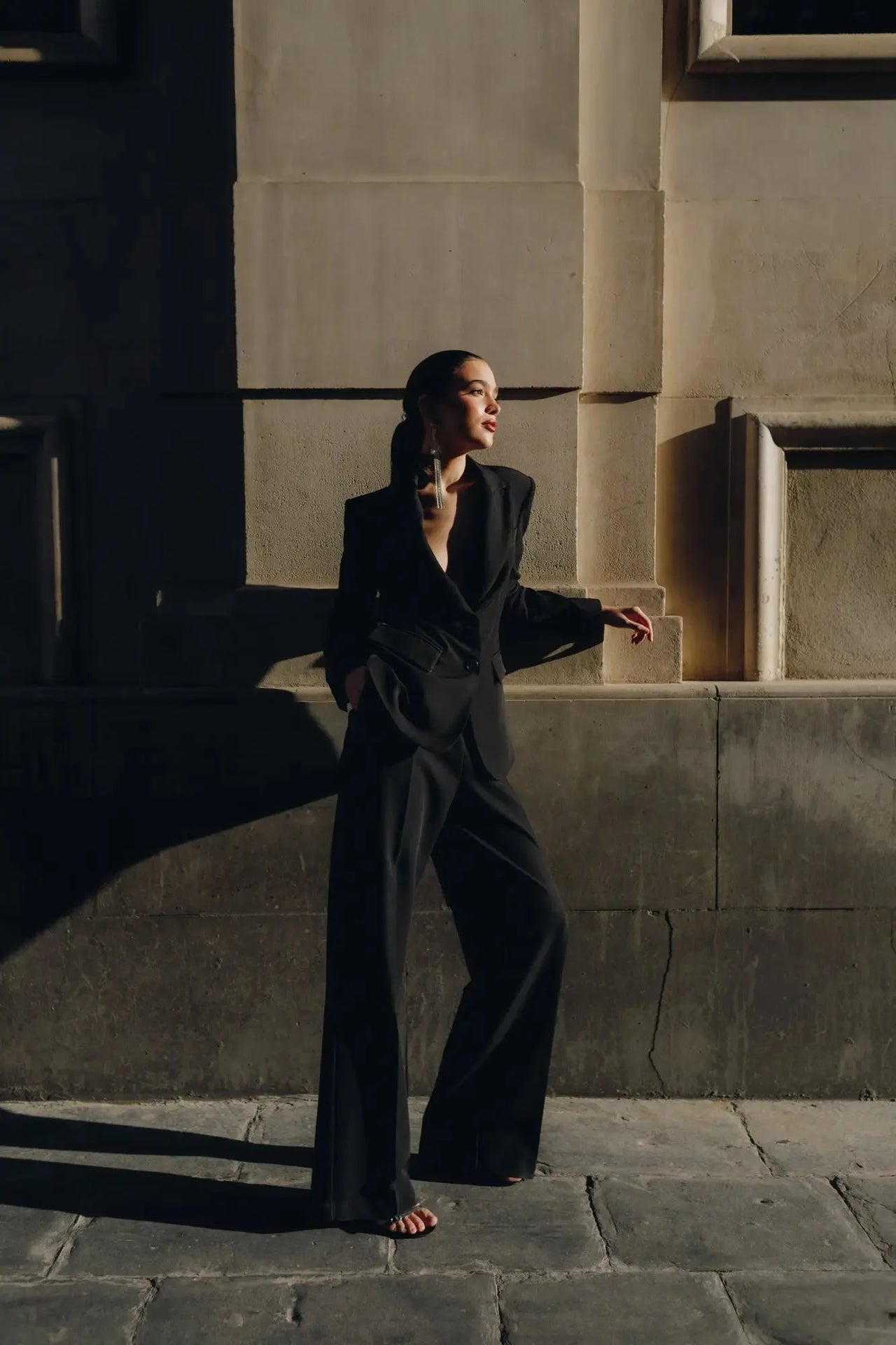 Modèle chic en Pantalon Noir Fluide Femme Élégant à Pinces en Polyester Recyclé, avec une tenue sophistiquée devant un mur moderne.