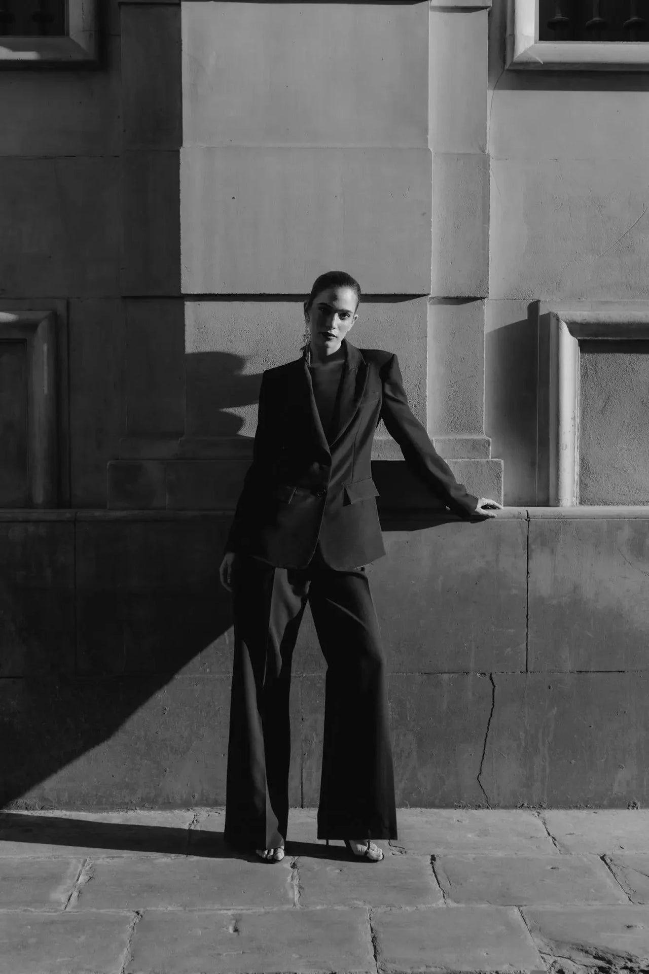 Pantalon Noir Fluide Femme Élégant à Pinces en Polyester Recyclé, modèle posant de manière frappante avec un éclairage dramatique.