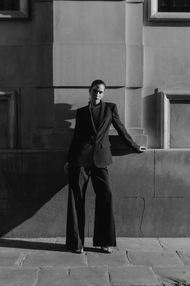 Pantalon Noir Fluide Femme Élégant à Pinces en Polyester Recyclé, modèle posant de manière frappante avec un éclairage dramatique.