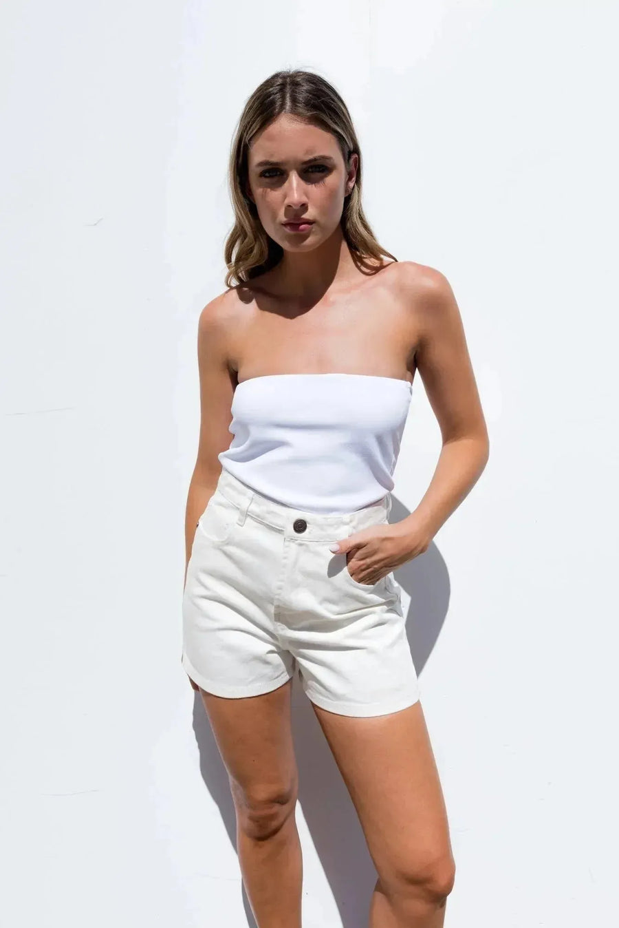 Modèle portant un ensemble haut blanc cassé et short beige taille haute, idéal pour l'été, mettant en avant le short en jean femme.