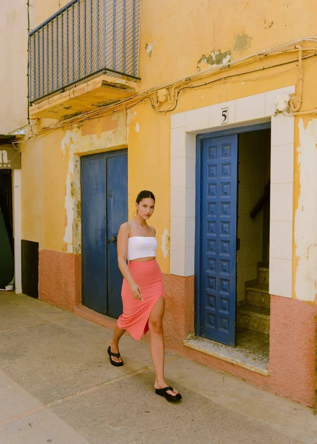 Femme portant une jupe midi rose corail en tissu fluide avec fente côté