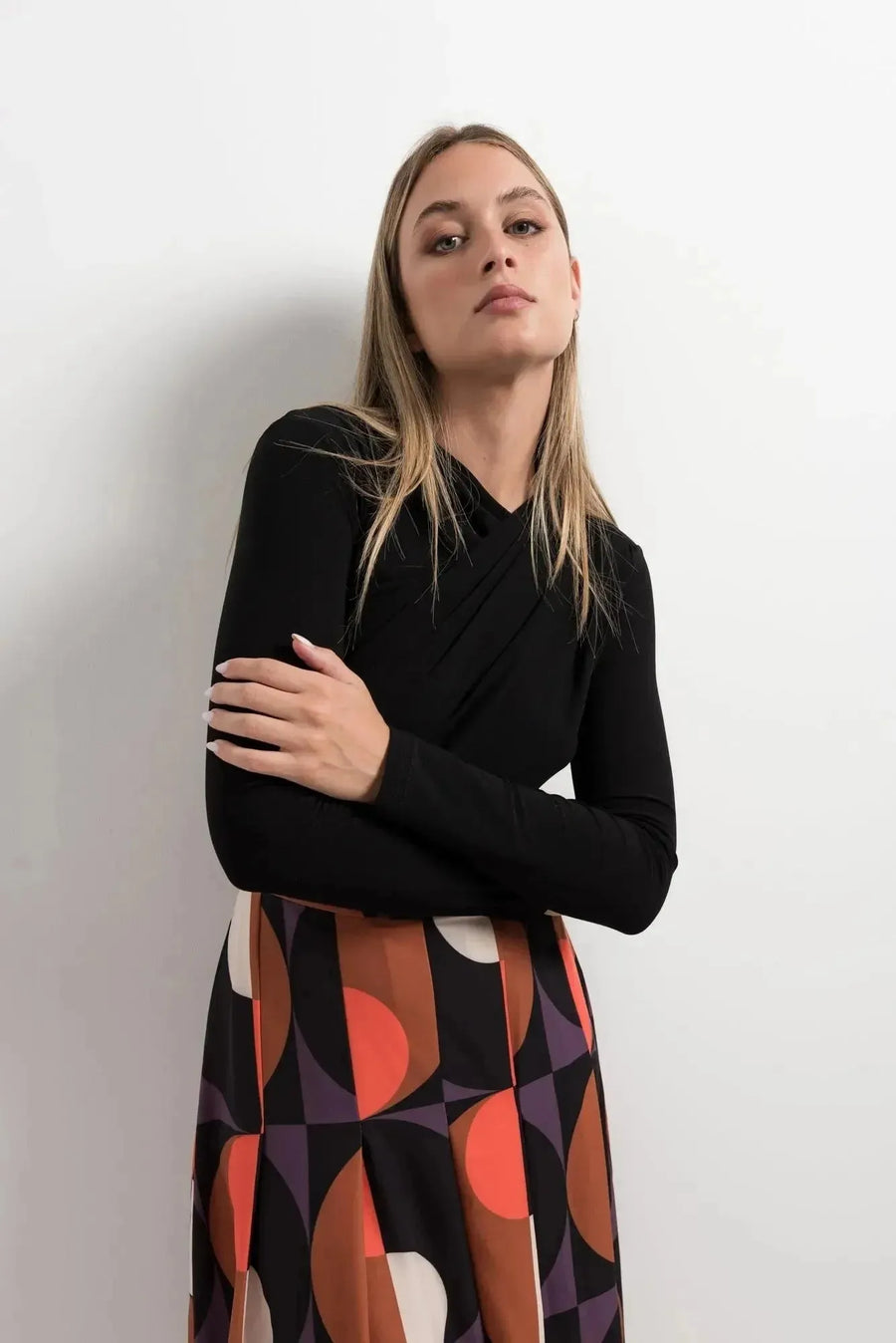 Gros plan sur une femme avec un haut noir, mettant en valeur la jupe plissée imprimée géométrique. Cette jupe année 70, avec ses motifs colorés, exprime un style affirmé et élégant.