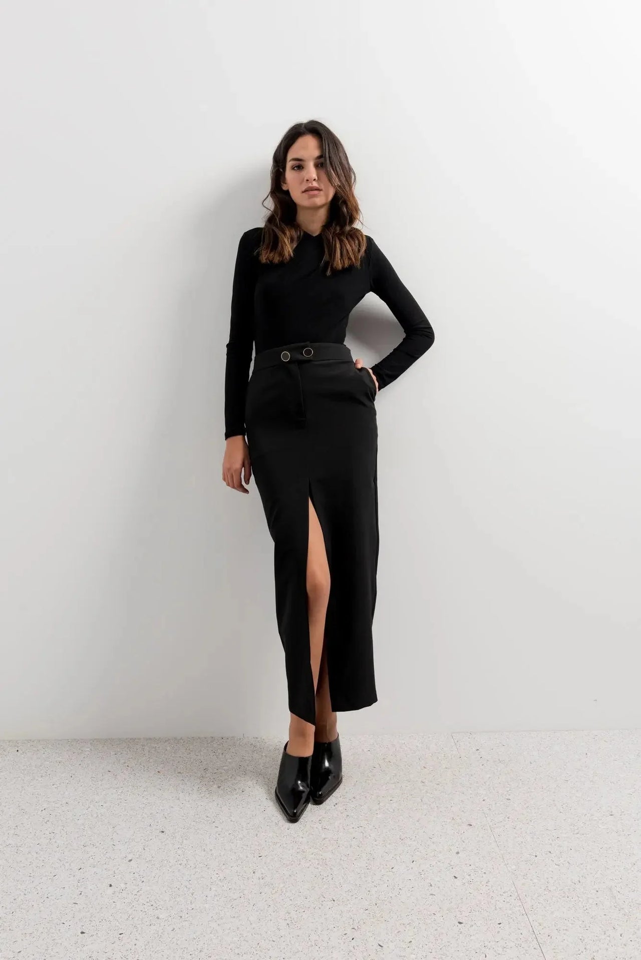 Femme stylée dans une jupe longue fendue devant, portant le modèle Jupe Boutonnée Midi Fendue Noir - Élégance Confortable Pour Toutes Occasions, debout avec confiance.