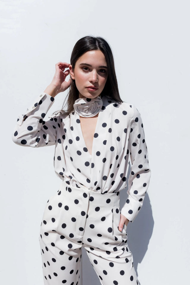 Femme portant un pantalon motif femme à pois noir et blanc, élégante avec des manches longues, devant un fond blanc.