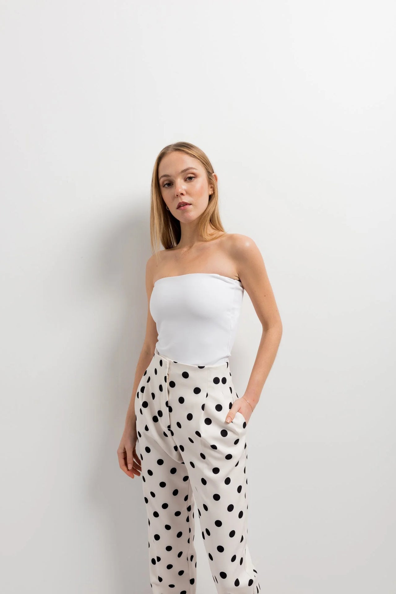 Femme posant en haut bandeau avec un pantalon motif femme à pois noir et blanc, affichant une silhouette moderne.