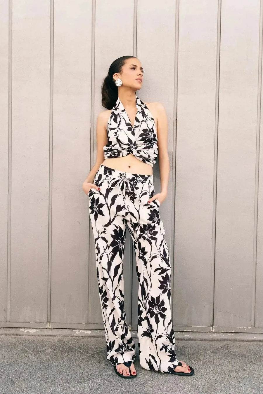 Mannequin affichant un style chic dans un pantalon fluide palazzo imprimé floral noir et blanc - taille élastiquée, légèreté et confort, les mains dans les poches. Pantalon à motif femme.
