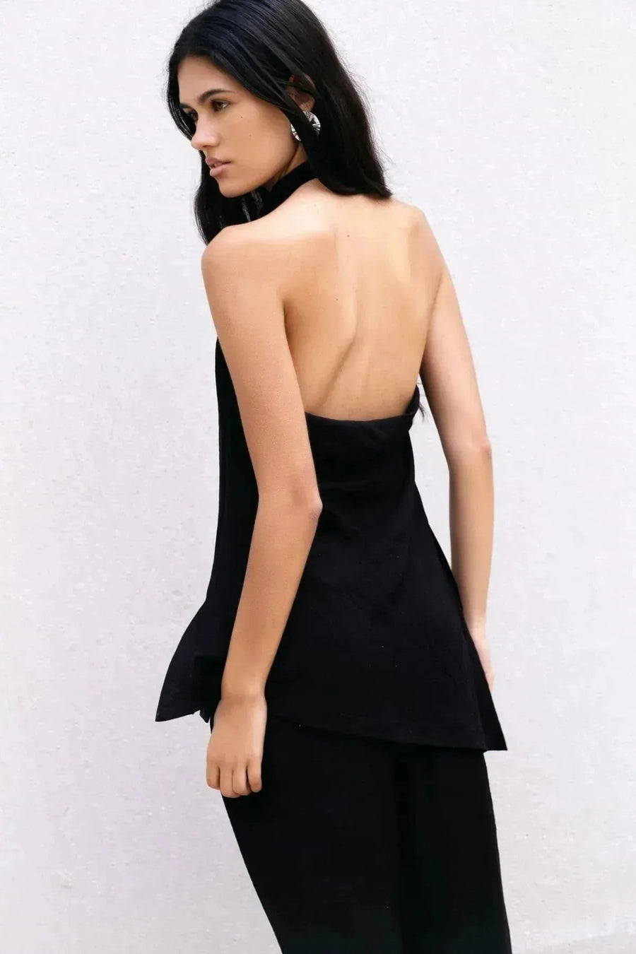 Femme vue de dos avec un top noir et un pantalon fluide noir taille haute, style élégant et contemporain, pantalon fluide femme.