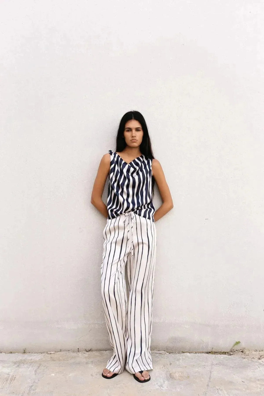 Femme portant un pantalon à rayures femme fluide et chic en satin léger, avec un top à rayures assorti, contre un mur neutre.