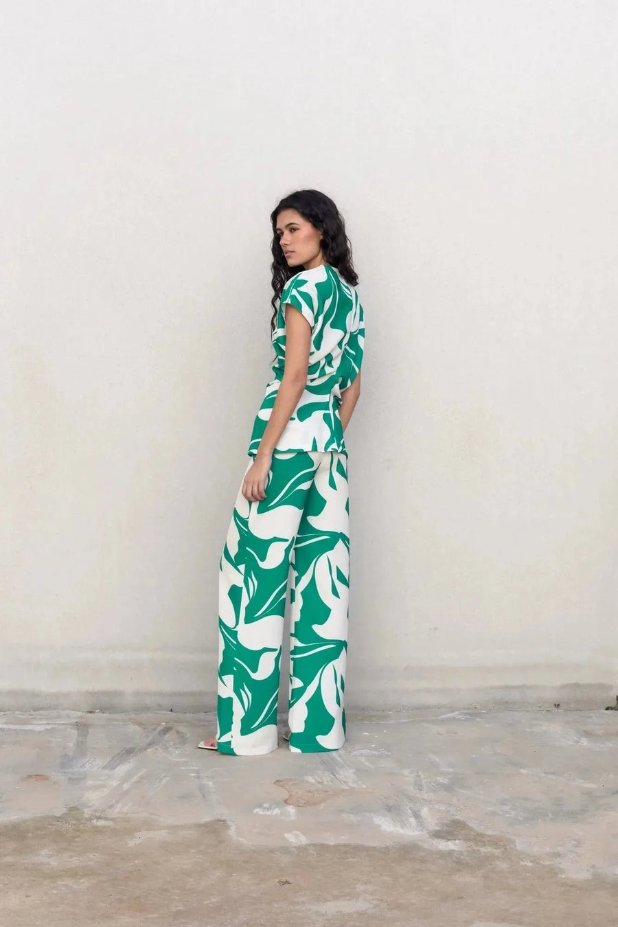 Femme vue de dos dans un ensemble pantalon palazzo imprimé floral vert et blanc, illustrant le pantalon palazzo femme avec un design original.