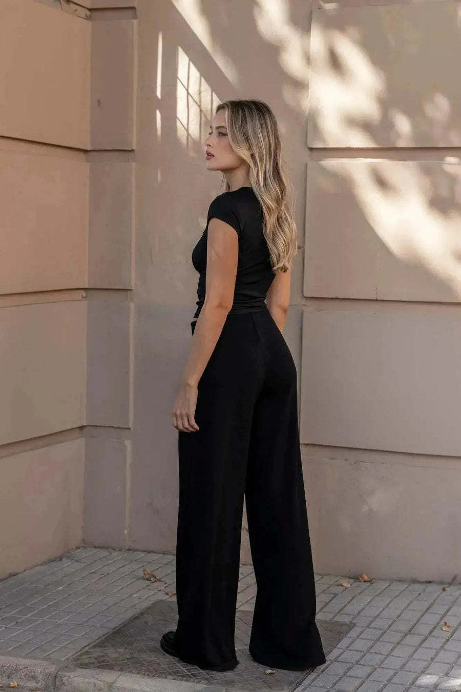 Femme vue de dos en t-shirt noir et pantalon large femme, illustrant un style contemporain et chic avec l'ensemble pull asymétrique.