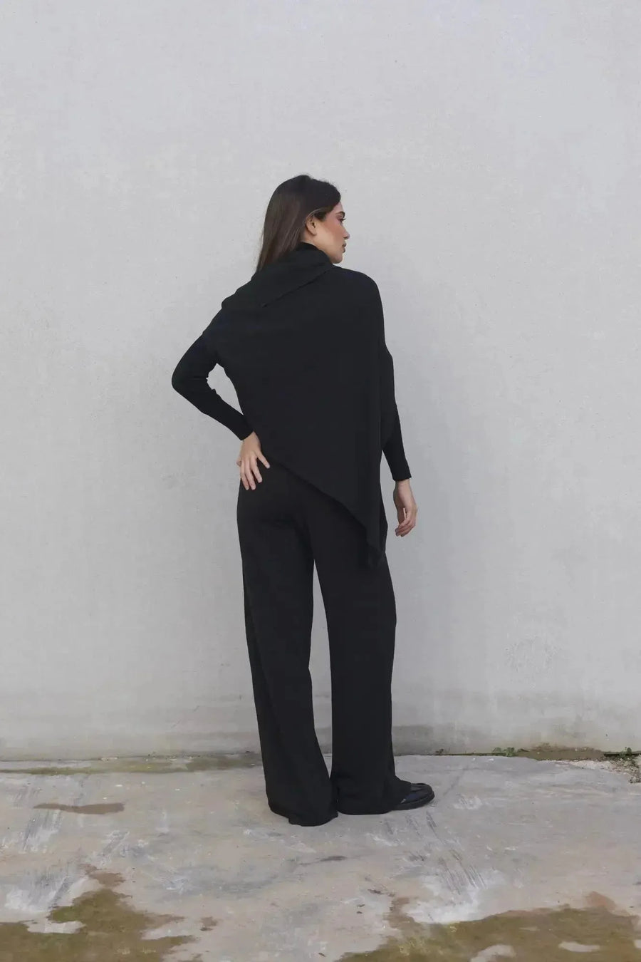 Femme de dos en ensemble pull asymétrique et pantalon à jambes larges, représentant le pantalon large femme en toute élégance.