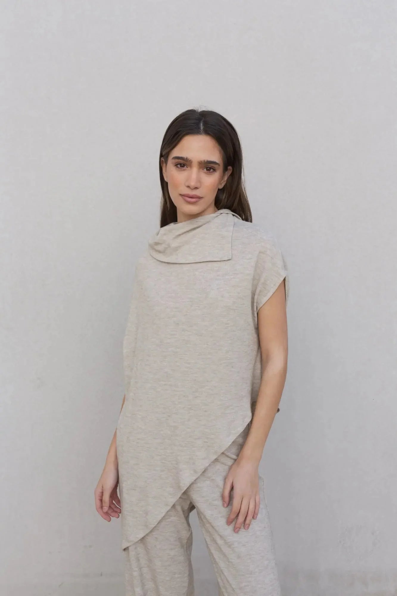 Femme portant un ensemble pull effet cape beige avec pantalon large et cowl neck