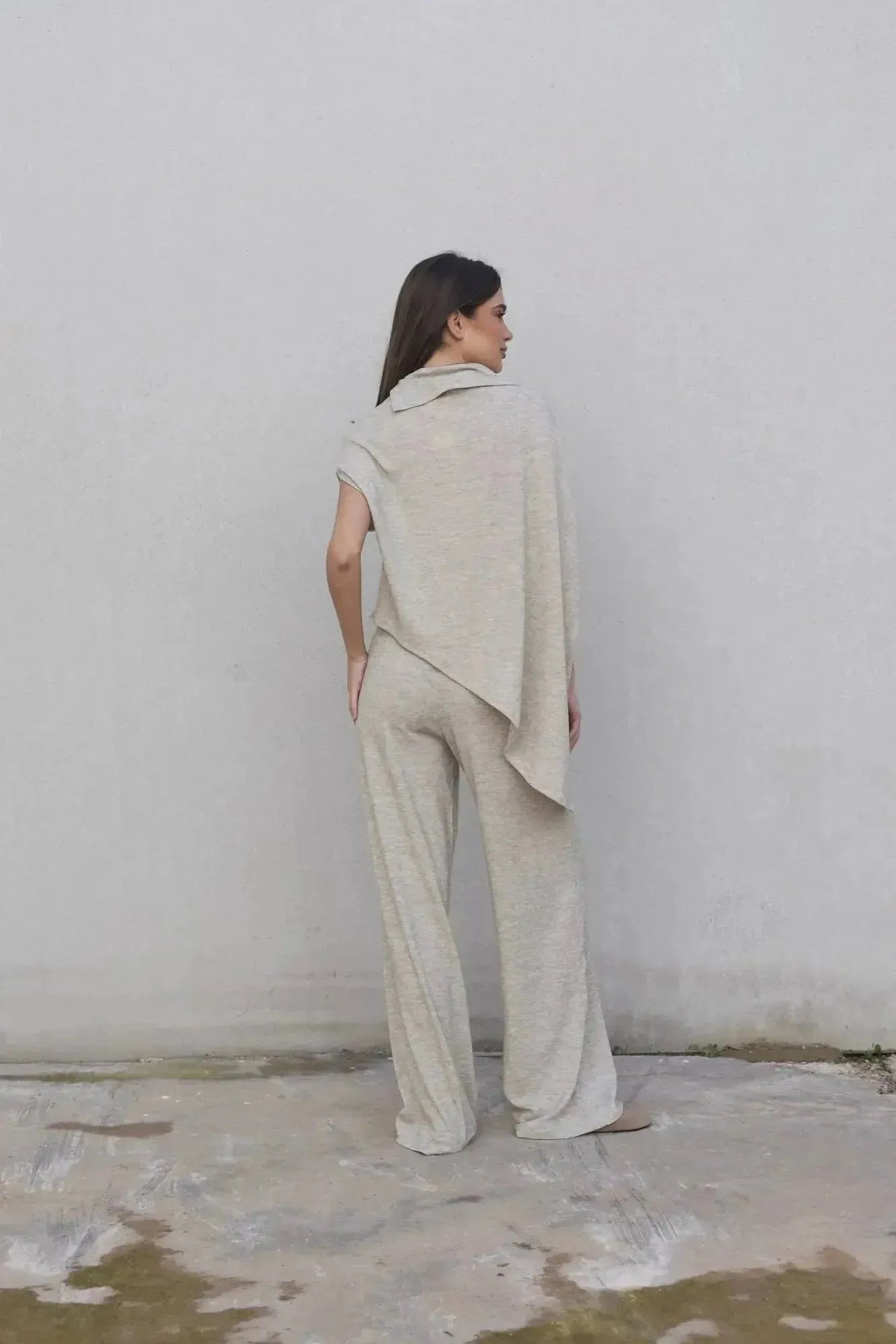 Femme portant un pull cape femme élégant beige avec pantalon large, vue de dos, idéal pour toutes occasions.