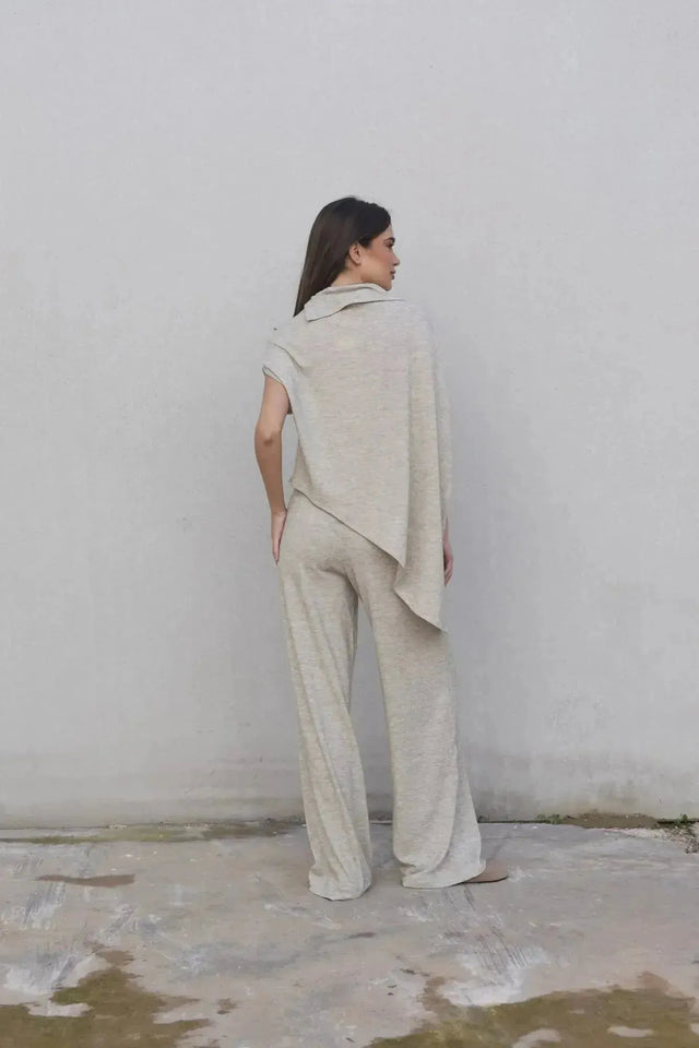 Femme portant un pull cape femme élégant beige avec pantalon large, vue de dos, idéal pour toutes occasions.