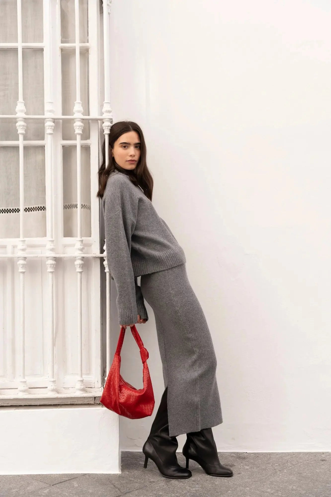 Femme portant un ensemble maille grise avec sac rouge et bottes noires