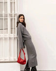 Femme stylée en jupe maille grise, confortable et élégante, avec une coupe ajustée mi-mollet, posant avec un pull gris et un sac rouge.