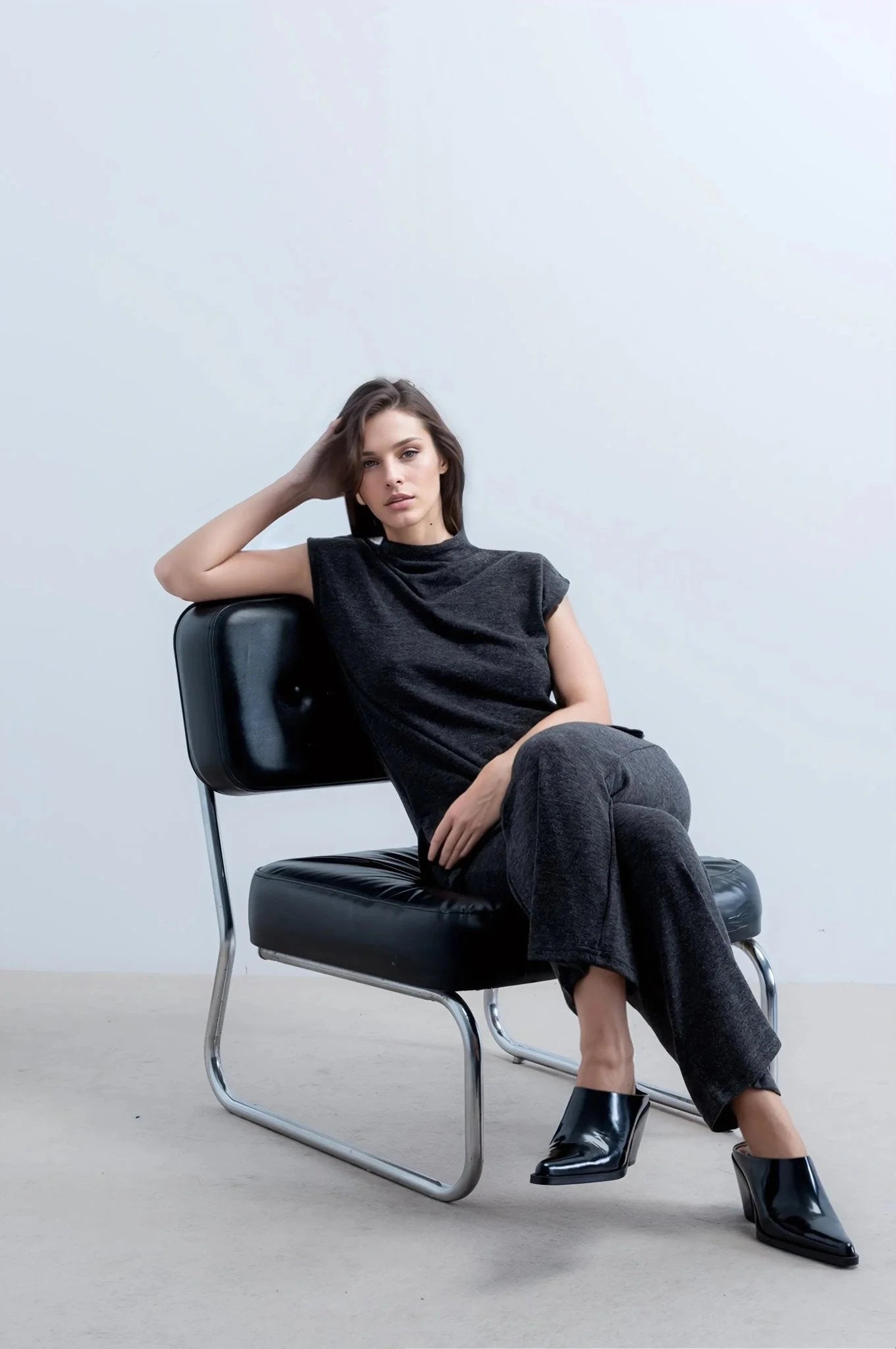 Femme en style tunique et pantalon large en tricot, assise dans un fauteuil en cuir noir