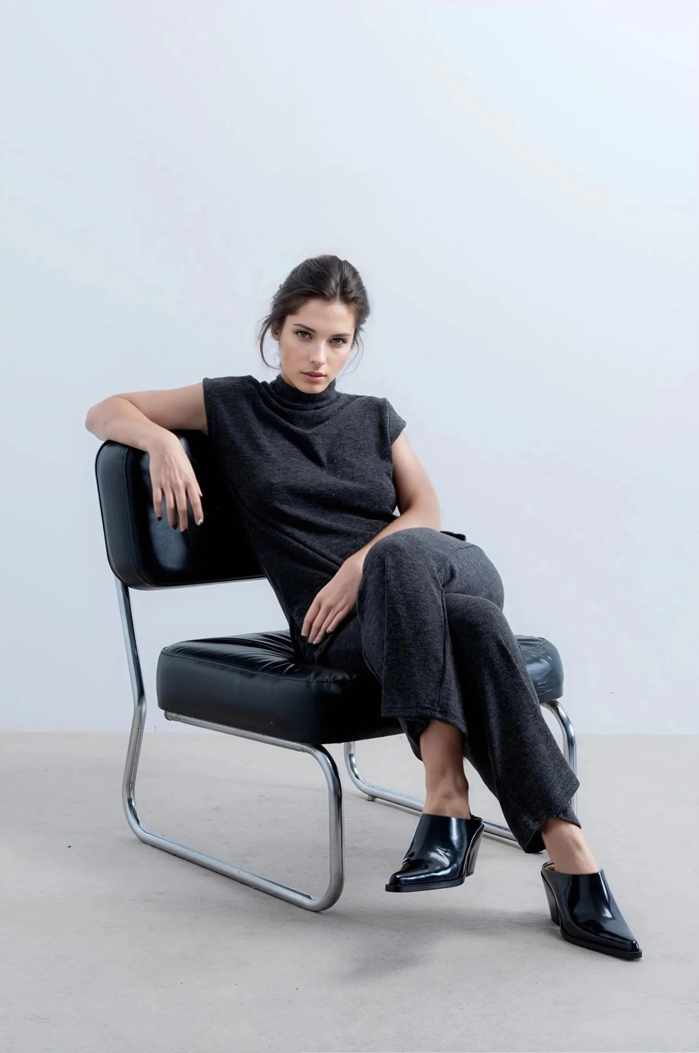 Femme en style tunique et pantalon large en tricot, assise en chaise en cuir noir