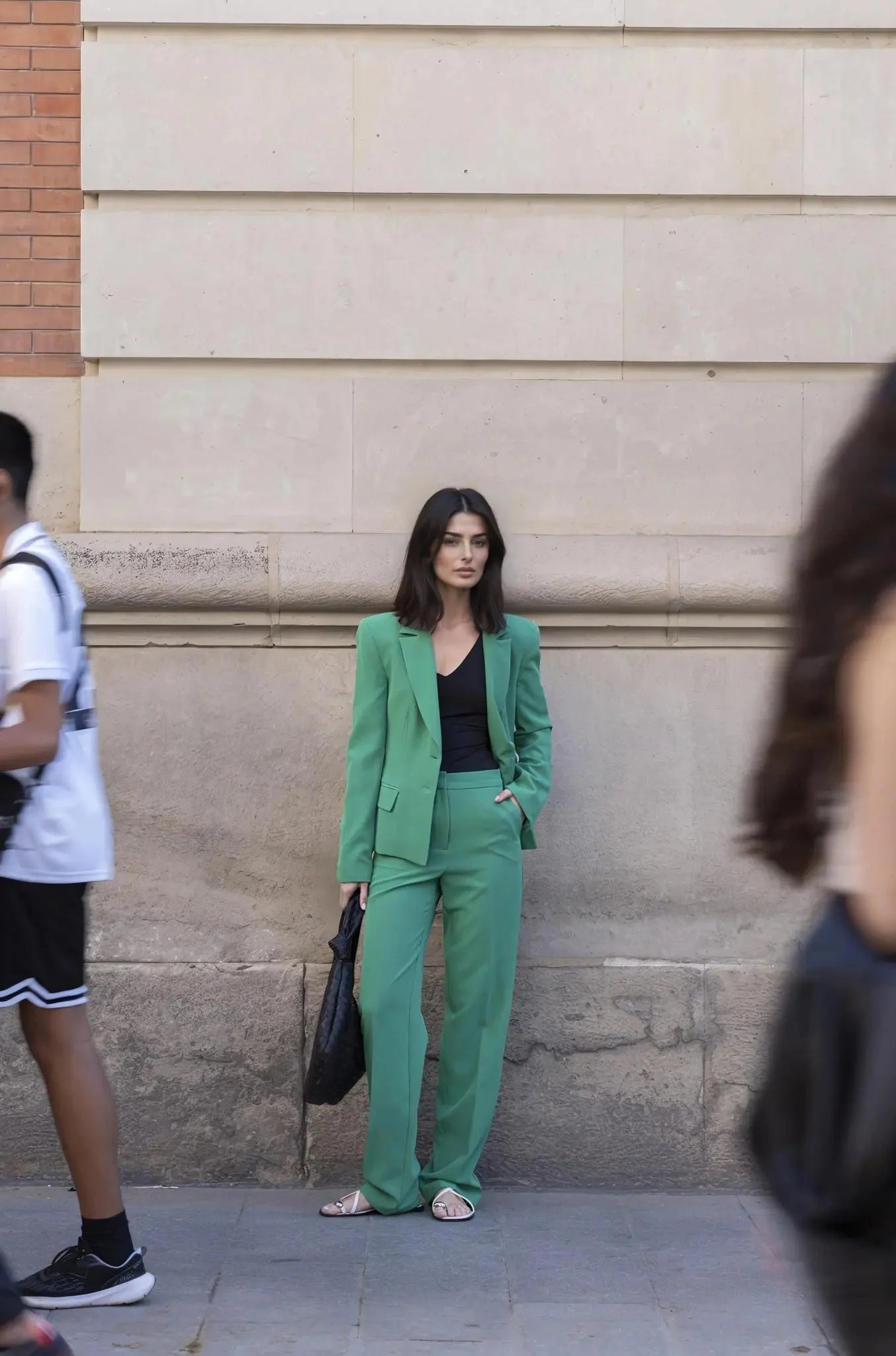 Femme en tailleur pantalon vert avec haut noir et sac à main noir