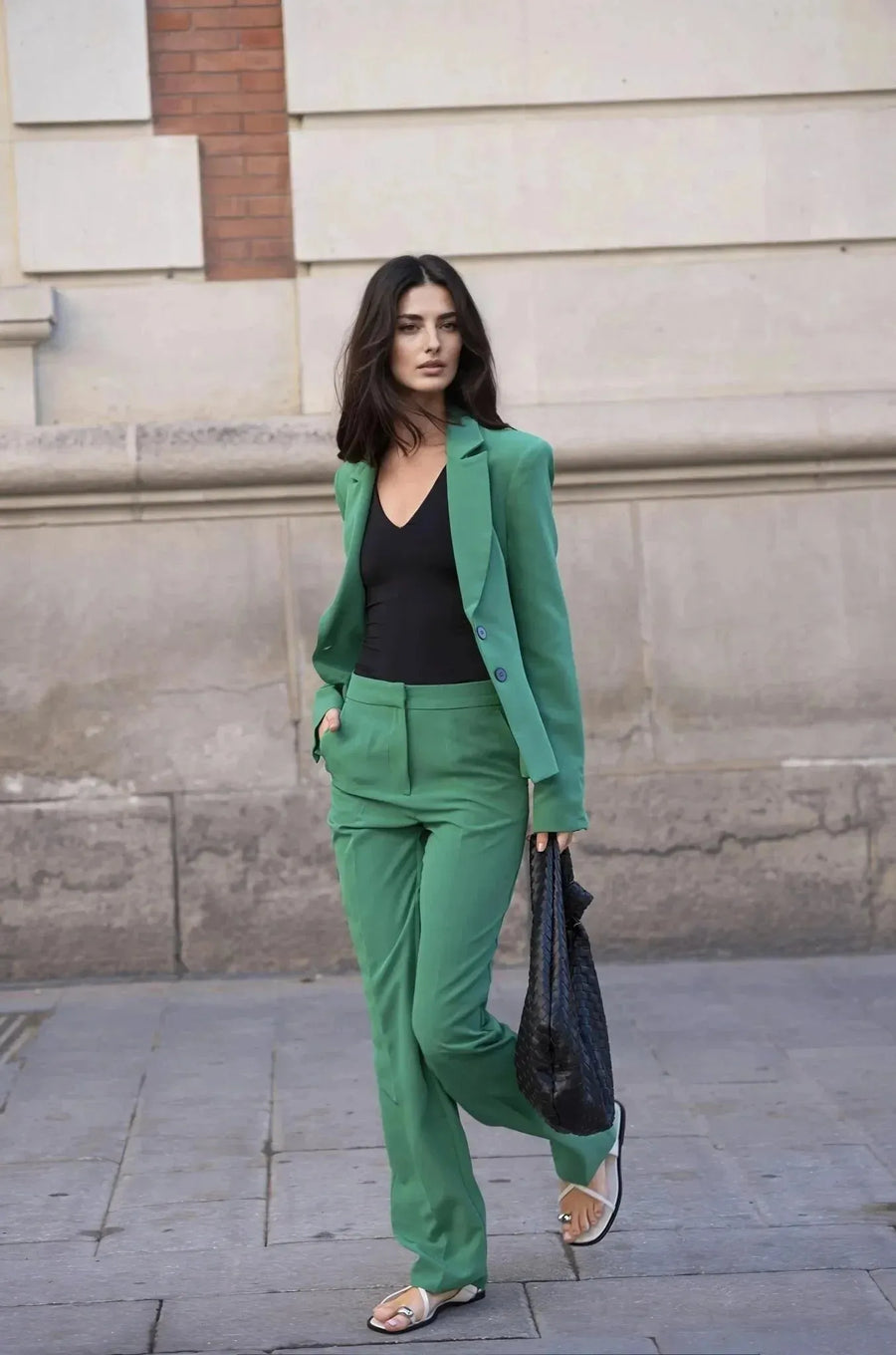 Femme professionnelle portant un ensemble tailleur pantalon vert femme, posant avec assurance devant un fond neutre.