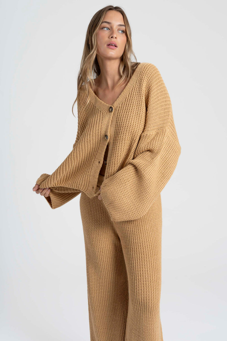 Femme debout mettant en avant l'ensemble maille femme italien en beige, avec un large pantalon et un col V.