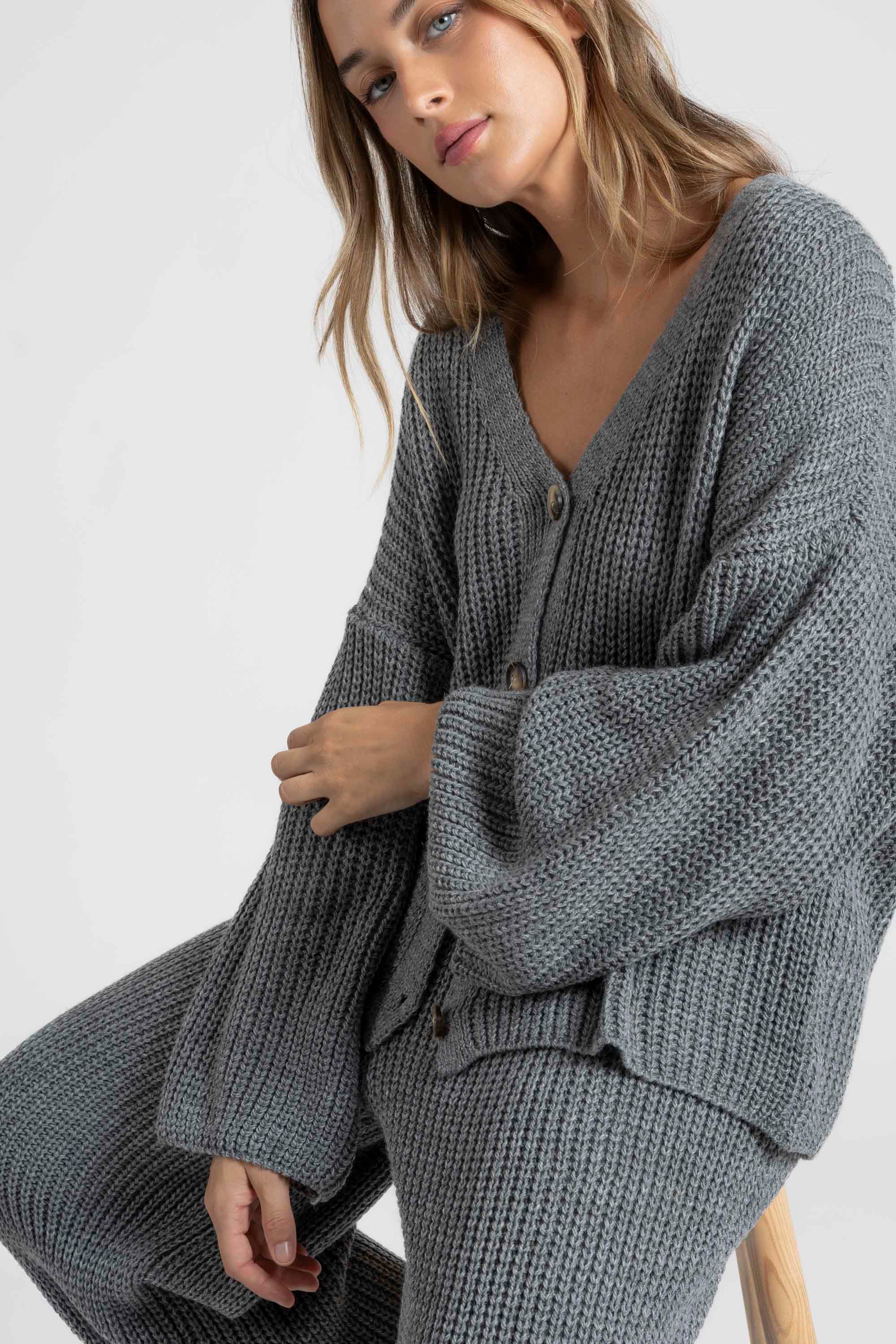 Femme assise dans un ensemble maille femme italien gris, avec un regard pensif, illustrant le style contemporain.