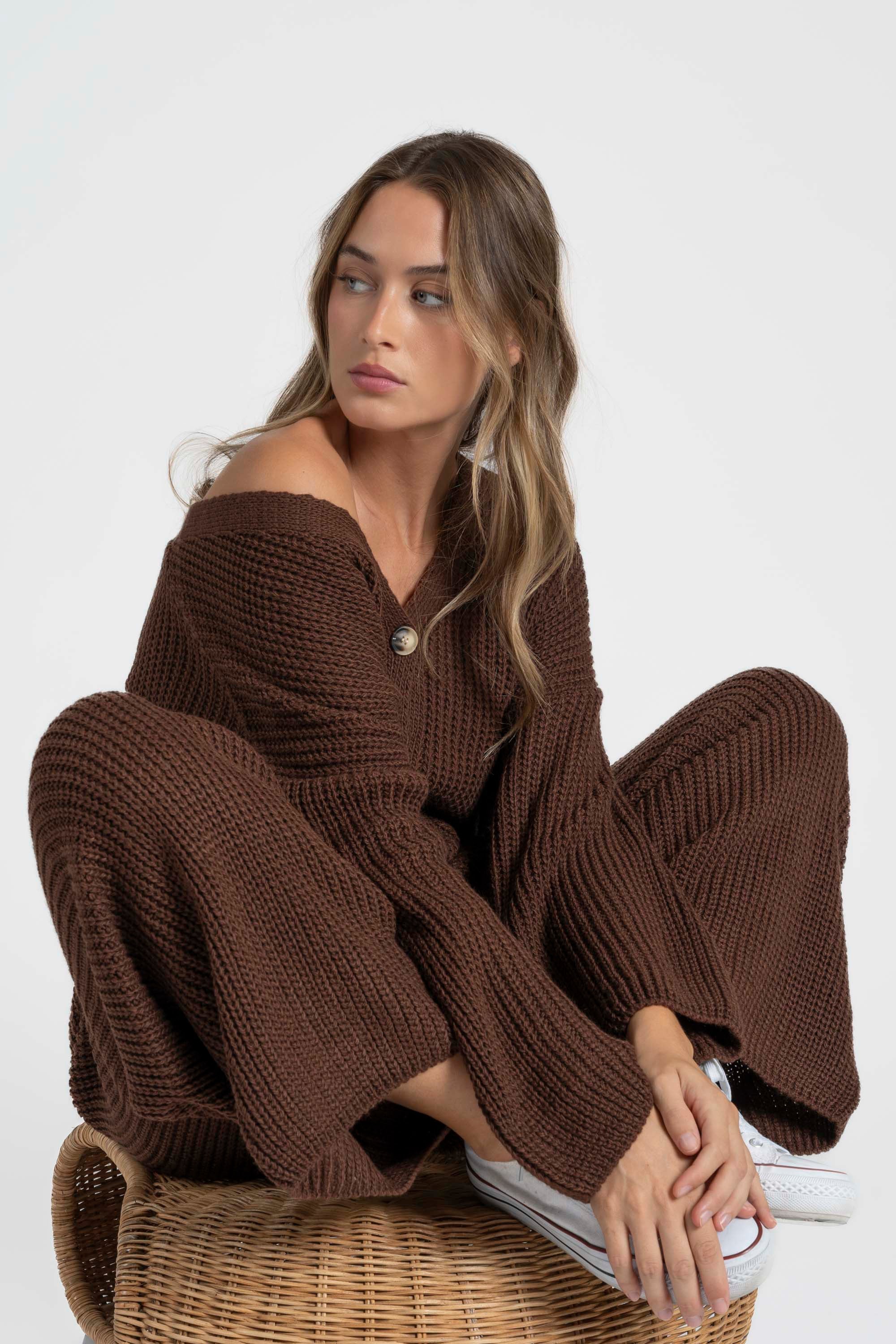 Femme dans un ensemble maille femme italien, style décontracté avec col V et pantalon large, assise sur un tabouret.