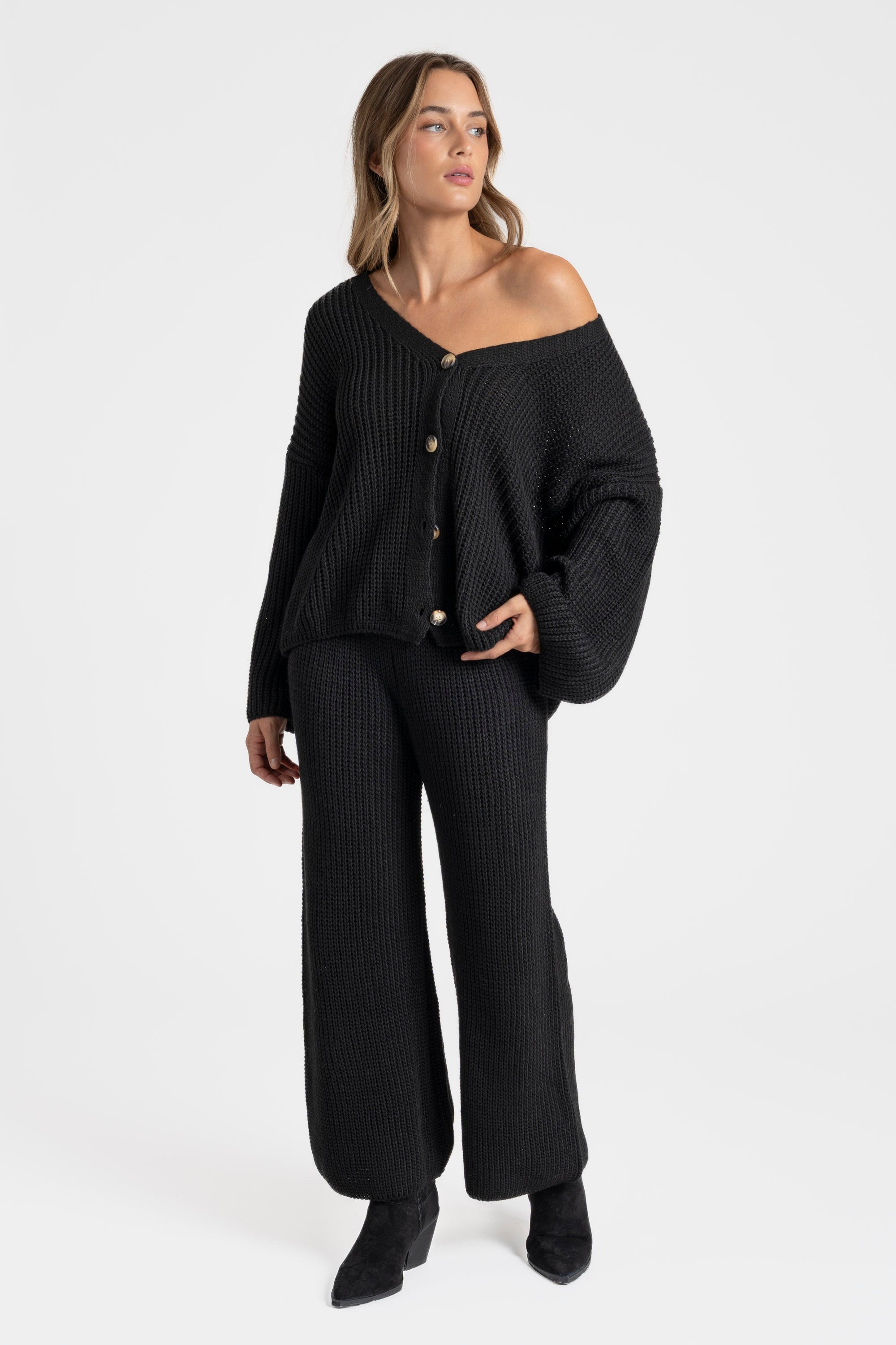 Femme élégante en ensemble maille femme italien, col V boutonné et pantalon large, se tenant debout sur un fond blanc.