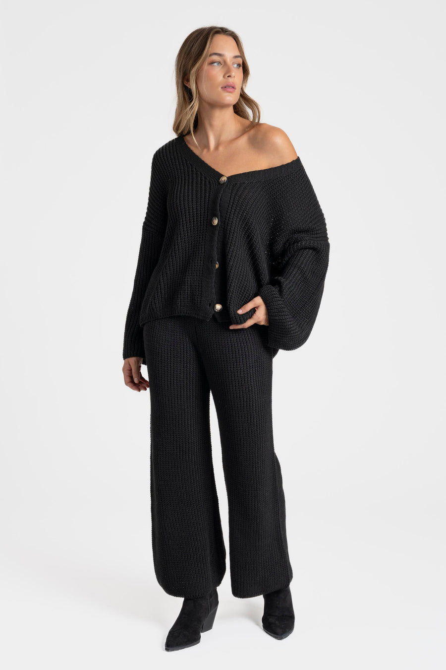 Femme élégante en ensemble maille femme italien, col V boutonné et pantalon large, se tenant debout sur un fond blanc.