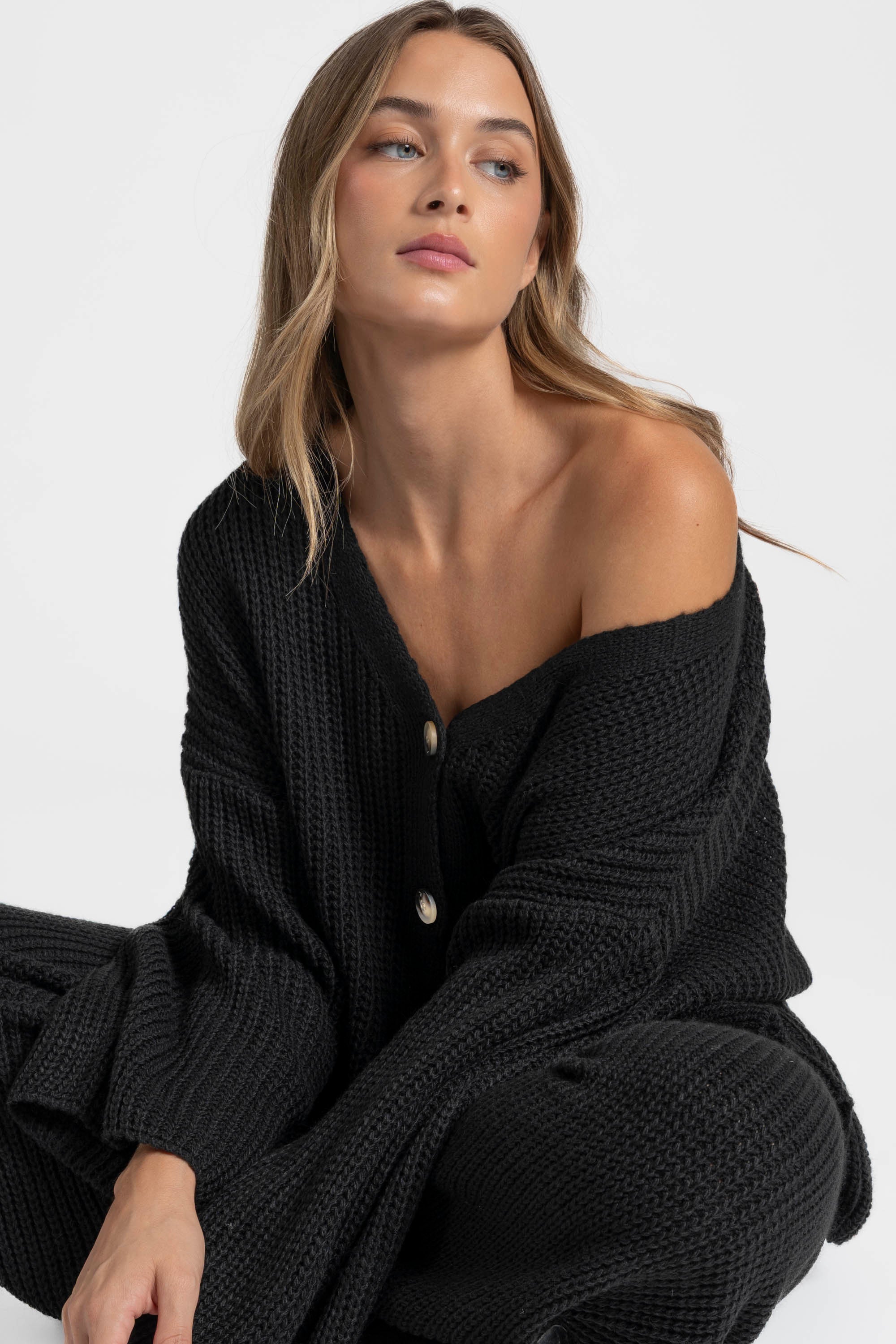 Femme avec un regard détendu, portant un ensemble maille femme italien en couleur noire, assise sur le sol.