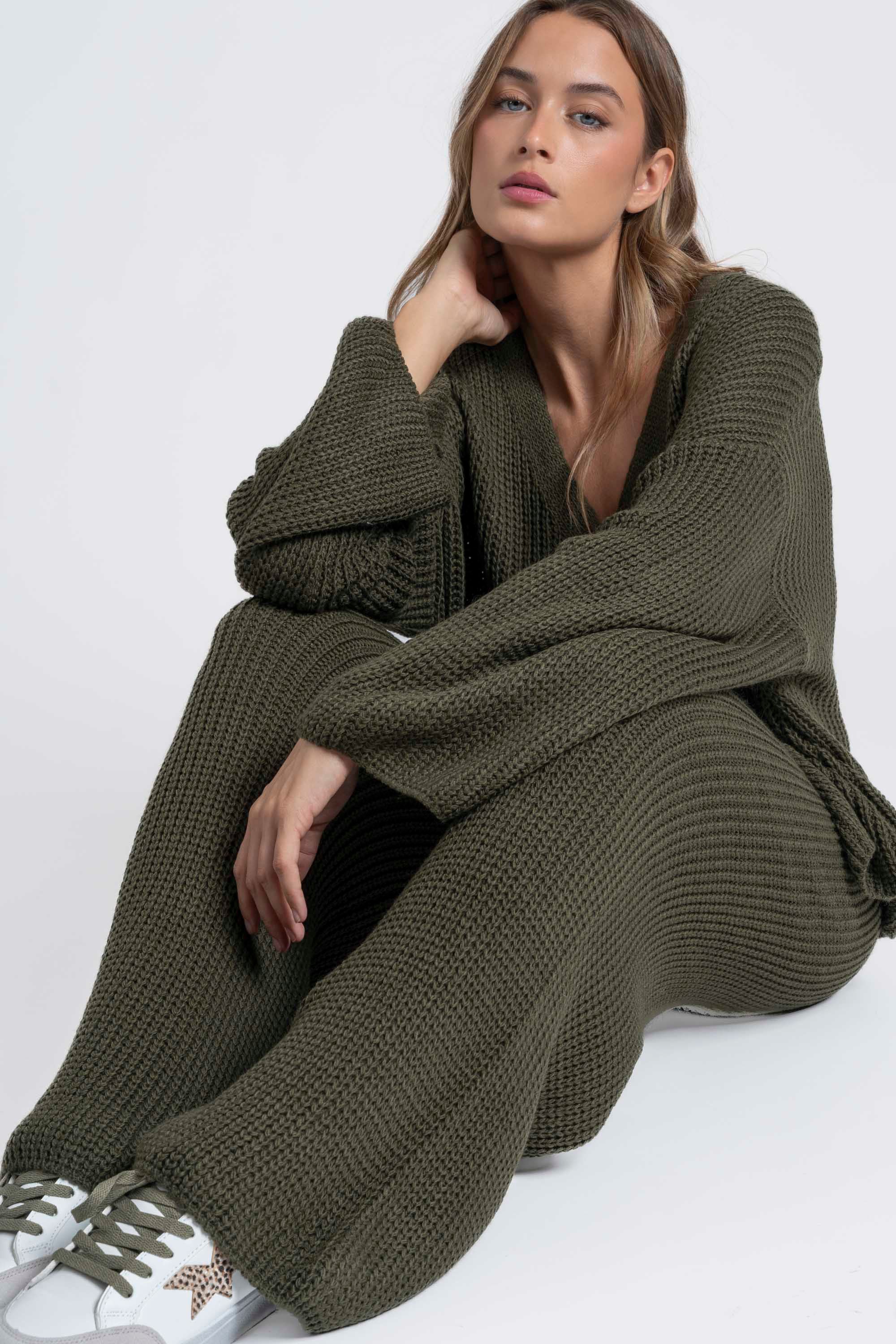 Femme assise, mettant en avant un ensemble maille femme italien couleur olive, avec une expression sereine.